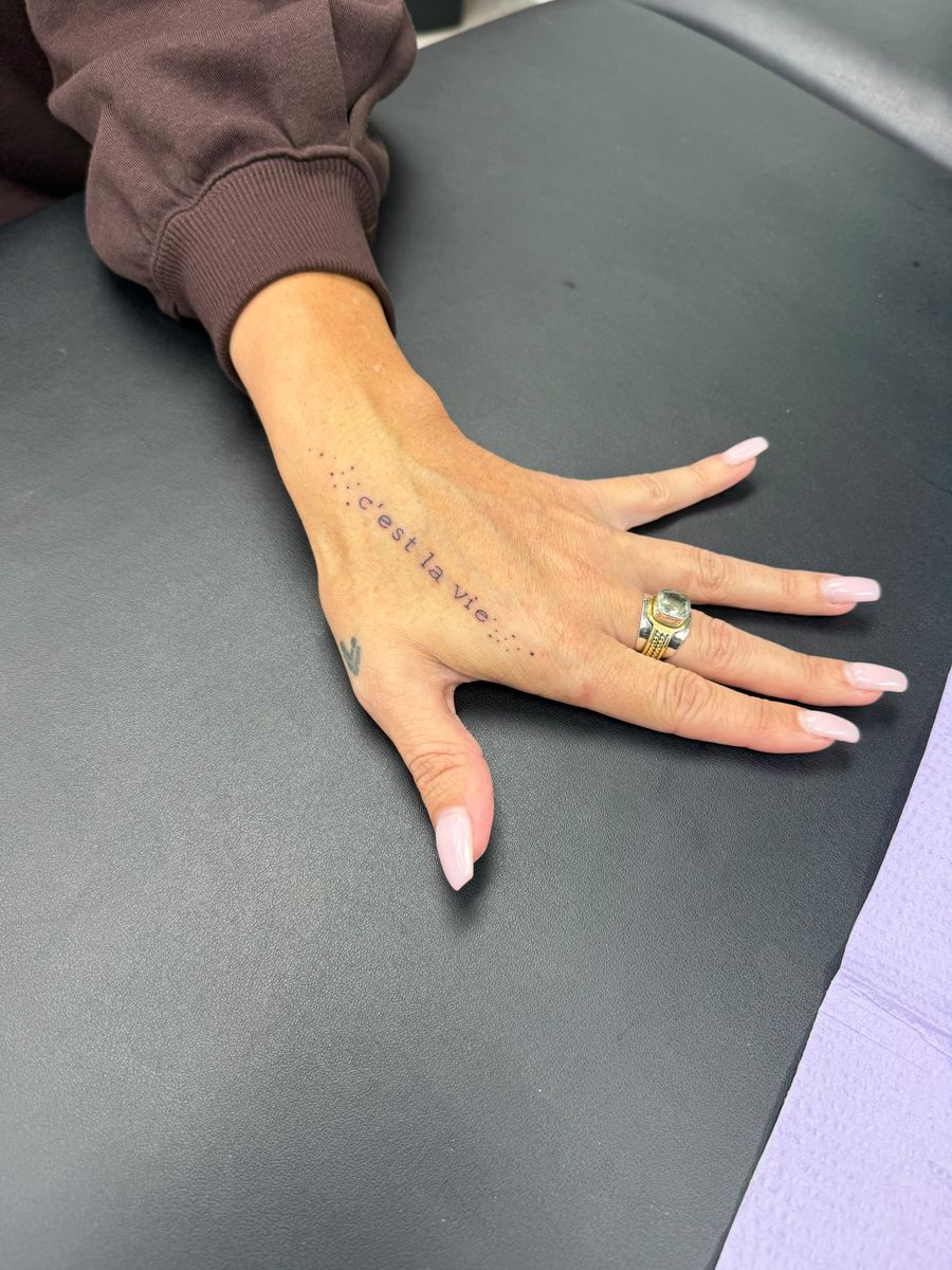 Delicate “c’est la vie” script on the side of the hand — fine line tattoo by Aline at Diamond Mind Tattoo, Buzzards Bay