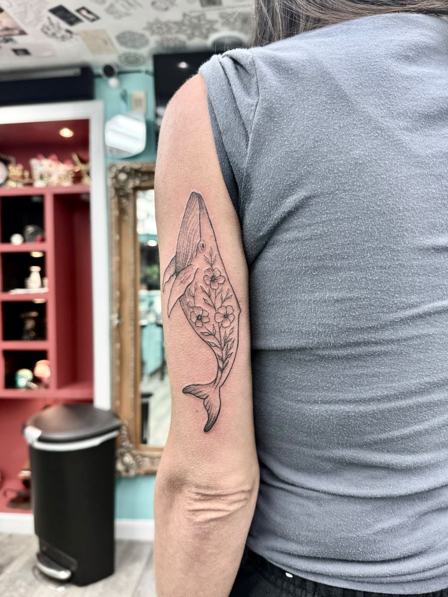 Whale filled with flowers on the back of the upper arm — fine line tattoo by Aline at Diamond Mind Tattoo, Buzzards Bay