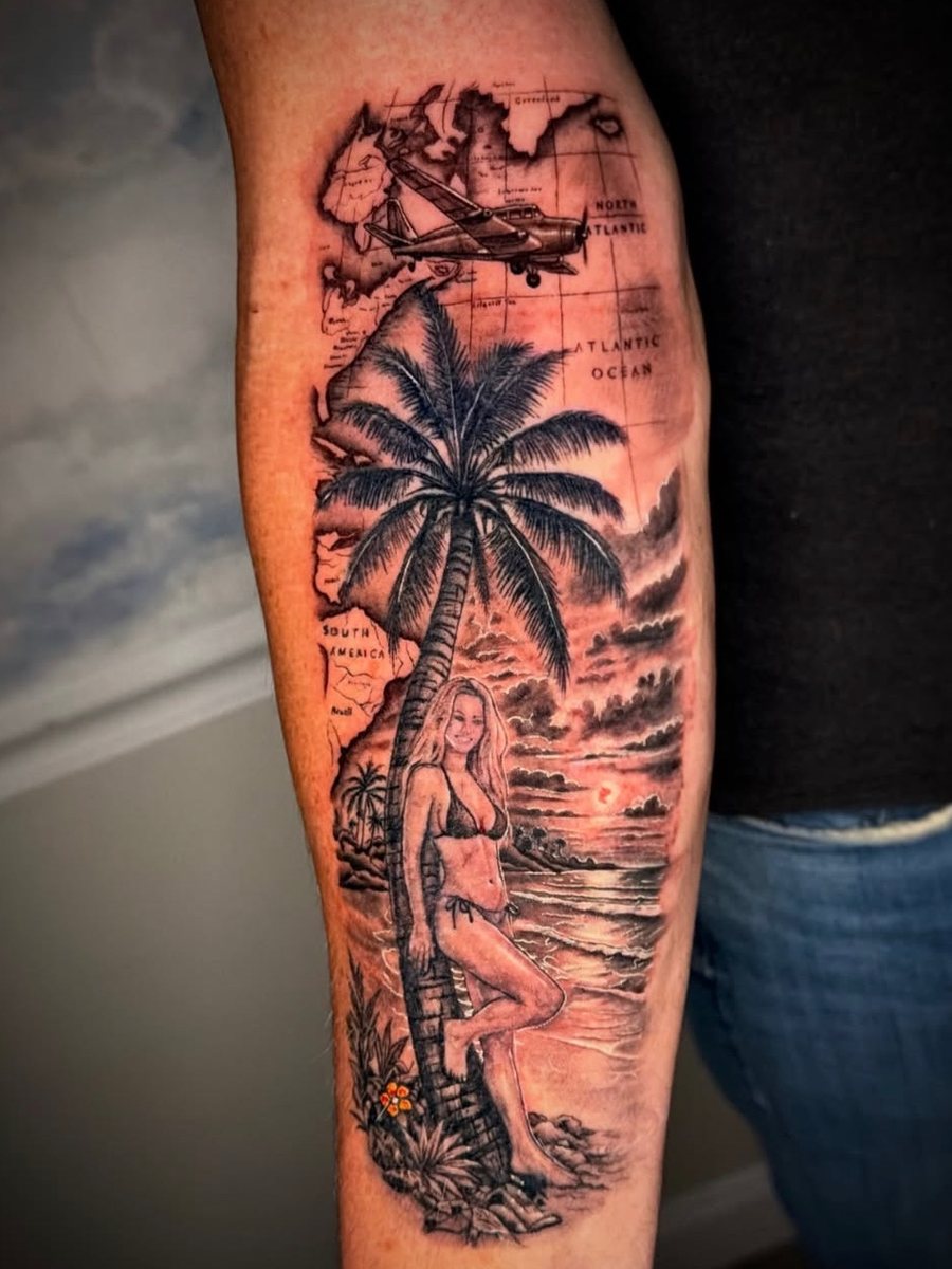 Forearm scene with a map of North and South America and the Atlantic, a small plane, a palm tree and a woman on the beach at sunset, black and grey realism tattoo by Brendon at Diamond Mind Tattoo, Buzzards Bay