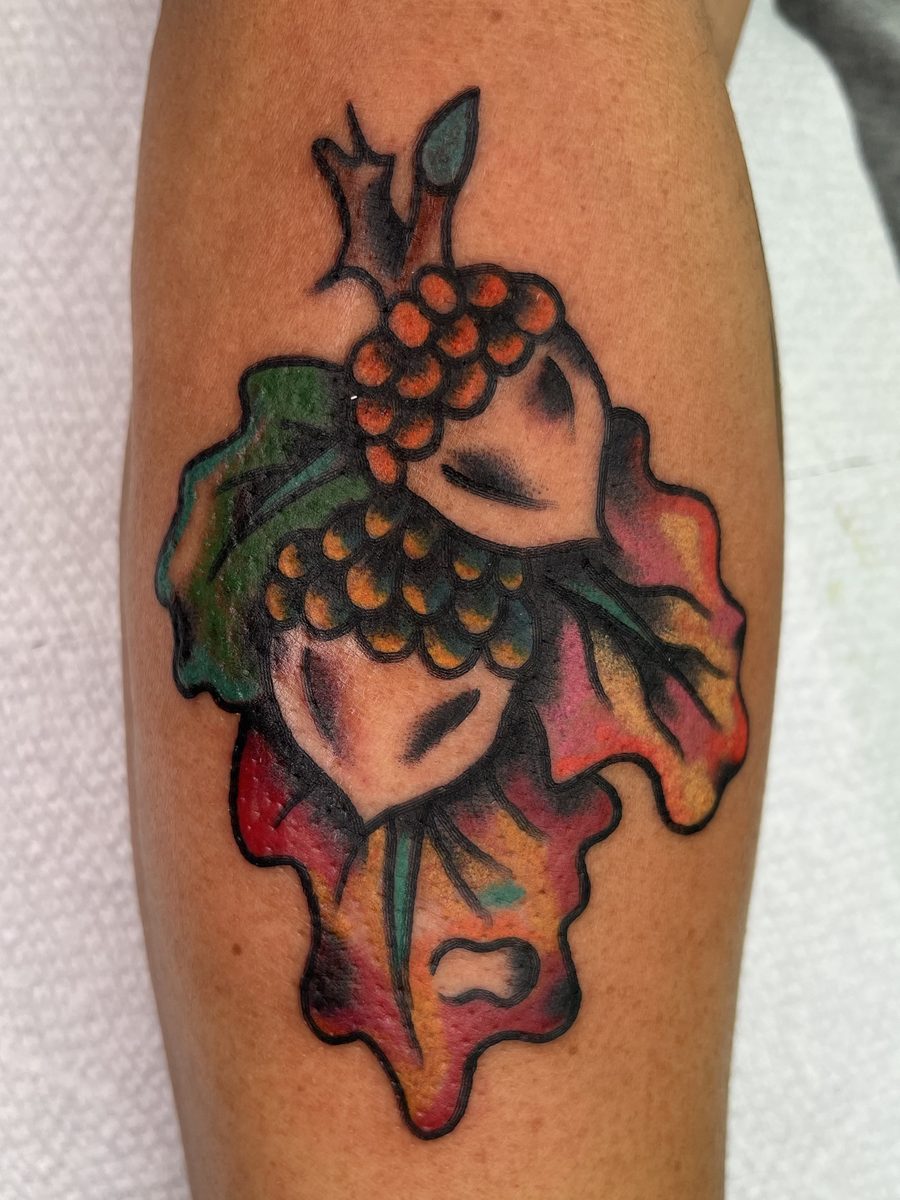 Acorns on an autumn oak leaf in red, orange and green on the forearm, American Traditional tattoo by Chris at Diamond Mind Tattoo, Buzzards Bay