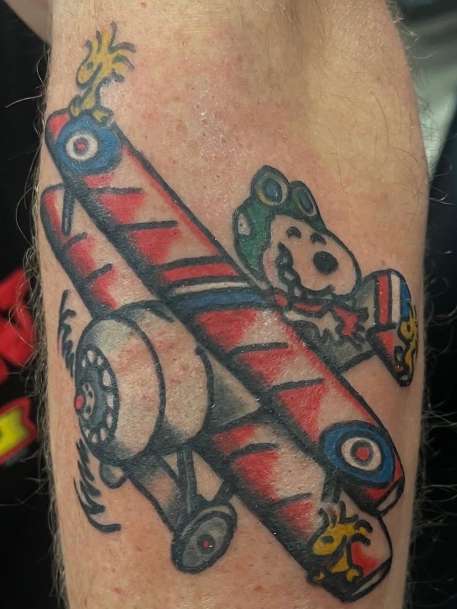Cartoon dog flying a red biplane with little yellow birds, American Traditional tattoo by Chris at Diamond Mind Tattoo, Buzzards Bay