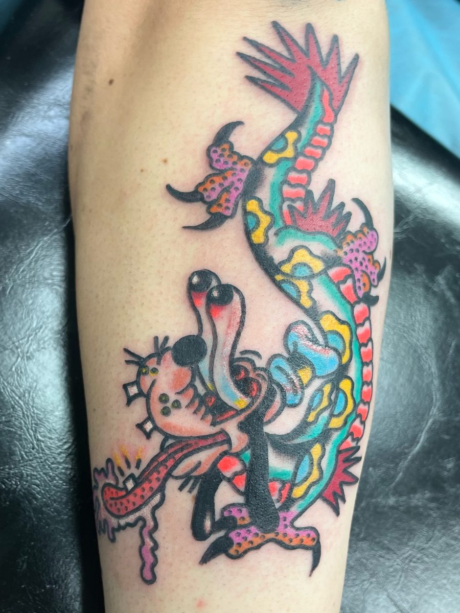 Dragon with a cartoon-style dog head in teal, pink and yellow on the forearm, American Traditional tattoo by Chris at Diamond Mind Tattoo, Buzzards Bay