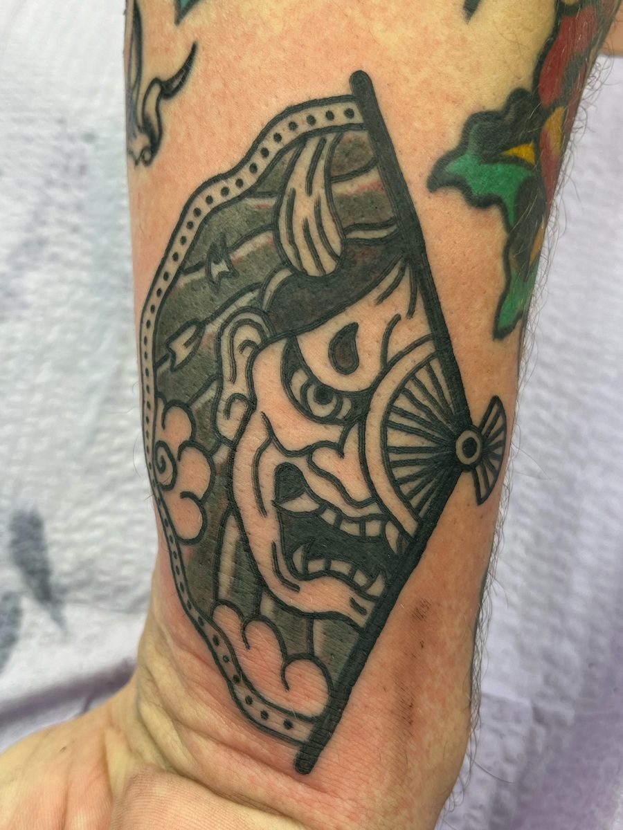 Japanese-style hannya mask inside a folding fan with clouds on the forearm near the wrist, black and grey tattoo by Chris at Diamond Mind Tattoo, Buzzards Bay